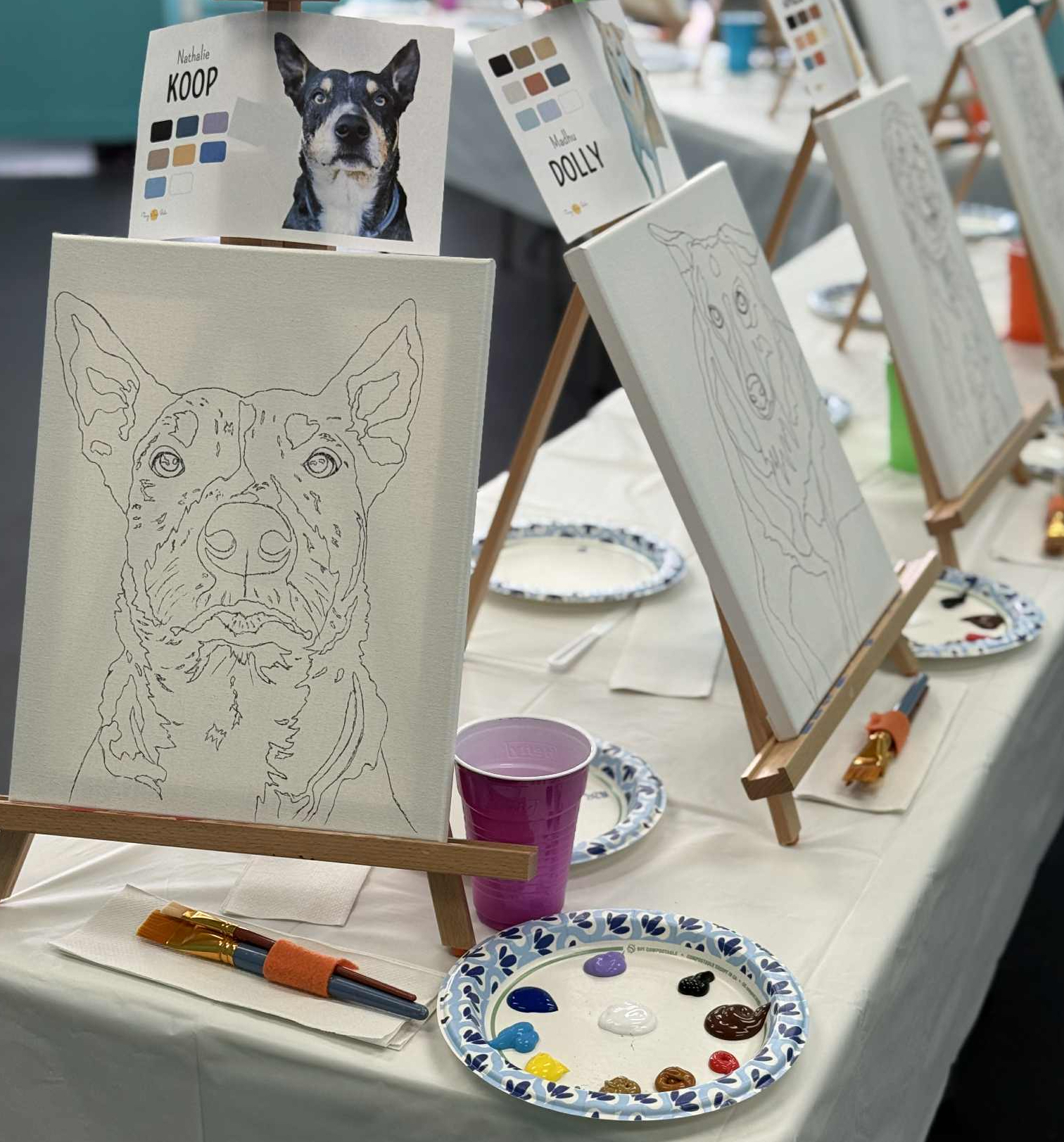 Easels with dog silhouette drawings and color swatches, painting supplies on a table in an art setup.